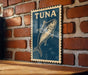 A blue sign with a fish illustration is mounted on a brick wall.