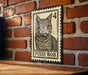 A metal sign featuring a cat illustration is mounted on a brick wall.