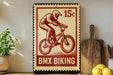 A vintage-style stamp featuring a person riding a bicycle, with the text "BMX Biking" printed on it. The stamp is placed on a wooden surface, with a potted plant, a cutting board, and some lemons nearby.