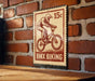 A vintage-style stamp featuring a person riding a bicycle, mounted on a brick wall.