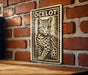 A wooden table with a metal plate featuring a black and white illustration of a cat, mounted on a brick wall.
