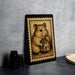 a framed illustration of a hamster holding a miniature house, placed on a countertop next to some black camera lenses.