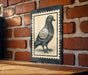 A black and white illustration of a pigeon is displayed on a brick wall, mounted on a wooden surface.