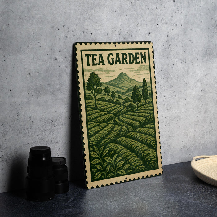 A metal sign with a green and white design depicting a tea garden, placed on a countertop next to some black camera lenses.