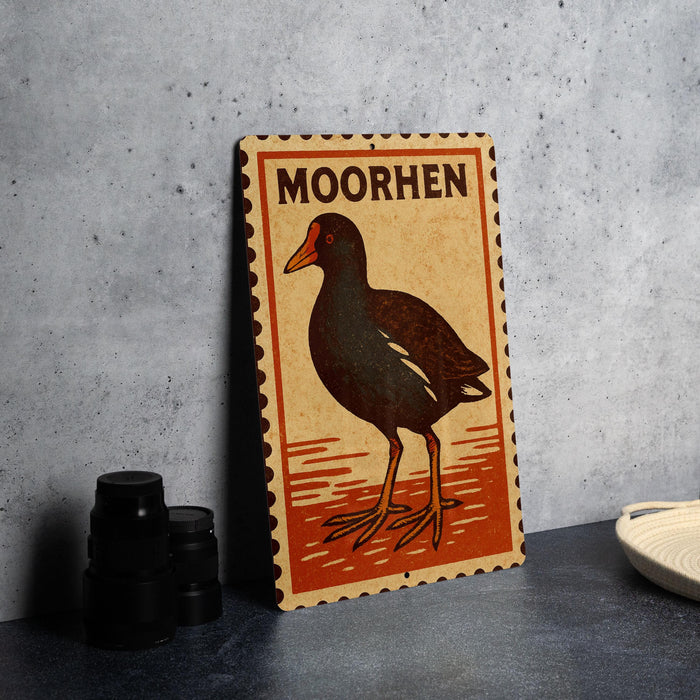 a wooden postcard with a bird illustration, placed on a table next to some black camera lenses.