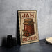 A metal sign with a jar of jam and the text "JAM PRESERVES" is displayed on a countertop.