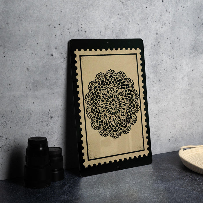 a framed black and white floral design on a black stand, placed on a dark surface against a gray background.