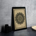 a framed black and white floral design on a black stand, placed on a dark surface against a gray background.