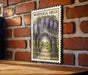 A framed illustration of a wisteria arch is displayed on a brick wall, with a wooden table below it.