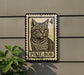 a metal sign with a cat illustration on it, mounted on a wall.