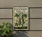 a sign with the text "CUCUMBER TRELLIS" and an illustration of two cucumbers growing on a vine. The sign is mounted on a wall, and there is a plant visible to the left of the sign.