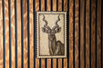 a close-up of a wooden wall with a framed image of a horned animal, likely a deer or antelope, prominently displayed on the wall.