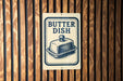 A sign that reads "Butter Dish" is displayed on a wooden wall.