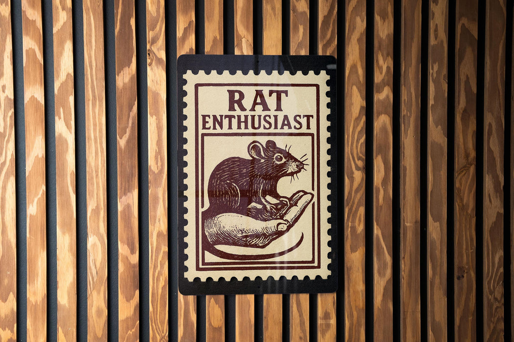 A sign with the word "RAT ENTHUSIAST" printed on it, featuring an illustration of a mouse on a hand.