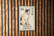 A Japanese bobtail cat is depicted on a postage stamp, which is affixed to a wooden wall.