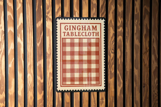 A red and white checkered tablecloth is hanging on a wooden wall.