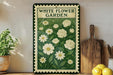 A vintage-style metal sign with a floral design, featuring white flowers and green leaves, is displayed on a shelf next to a wooden cutting board and a potted plant.