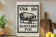 A sign with a pig illustration and text, mounted on a wall next to a wooden cutting board and some kitchen utensils.