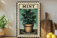 A framed illustration of a potted mint plant is displayed on a shelf, accompanied by a wooden cutting board and a bunch of lemons.