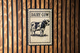 a metal sign with a cow illustration, mounted on a wooden wall.