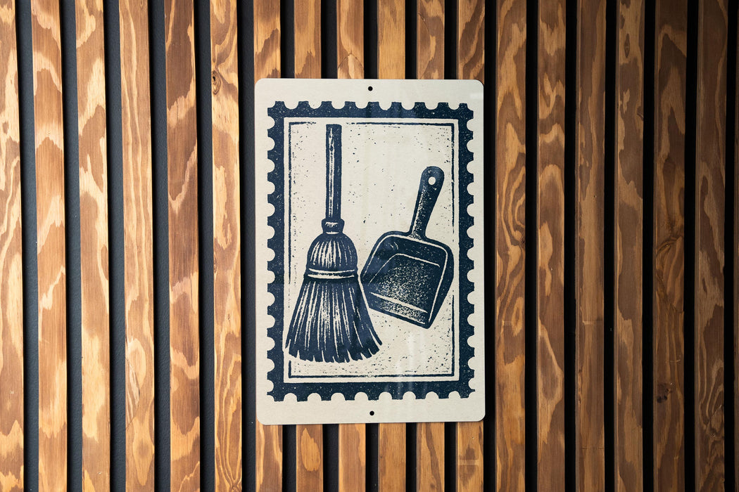 A sign with a black and white illustration of a broom and a dustpan is mounted on a wooden wall.