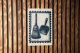 A sign with a black and white illustration of a broom and a dustpan is mounted on a wooden wall.