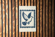 A sign featuring a blue bird in flight, with a postage stamp-like border, is displayed on a wooden wall.