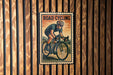 A vintage-style road cycling poster is displayed on a wooden wall, featuring a cyclist in action.