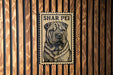 A metal sign with a stamp-like design featuring a dog's face is mounted on a wooden wall.