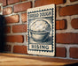 A sign with the text "BREAD DOUGH RISING" is displayed on a brick wall, with a wooden table below it.