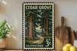 A vintage-style postage stamp depicting a forest scene, with the text "Cedar Grove" and "U.S. Postage 3c" printed on it. The stamp is displayed on a shelf next to a wooden cutting board and a potted plant.