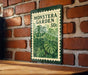A metal sign with a stamp-like design hangs on a brick wall, featuring a large image of a monstera plant.