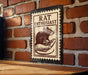 A metal sign with a stamp-like design hangs on a brick wall, featuring a mouse and the text "RAT ENTHUSIAST".