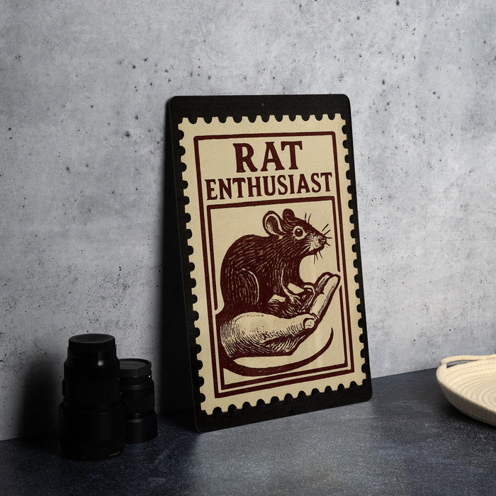 A framed poster with a rat illustration and the text "RAT ENTHUSIAST" is displayed on a table.