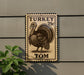 A wooden sign with a turkey stamp design, mounted on a wall.