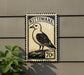 A postage stamp featuring a bird, likely a Kittiwake, is mounted on a wall.