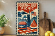 A vintage-style metal sign with a picnic scene, featuring a hamburger, watermelon slice, and a picnic table, along with an American flag and a wooden cutting board.