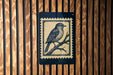 A postage stamp featuring a bird perched on a branch is displayed on a wooden wall.