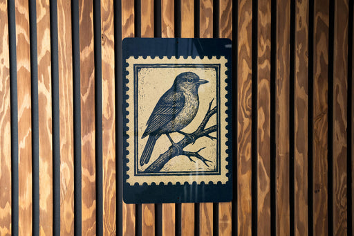 A postage stamp featuring a bird perched on a branch is displayed on a wooden wall.