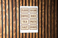 A sign with the names of various food items written on it, mounted on a wooden wall.