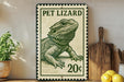 A metal sign featuring a drawing of a pet lizard, with the text "PET LIZARD" and "20¢" printed on it. The sign is placed on a wooden surface, with a potted plant, a wooden cutting board, and some lemons nearby.