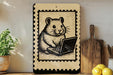 a wooden board with a black and white illustration of a hamster sitting on a laptop, surrounded by various kitchen utensils and a potted plant.