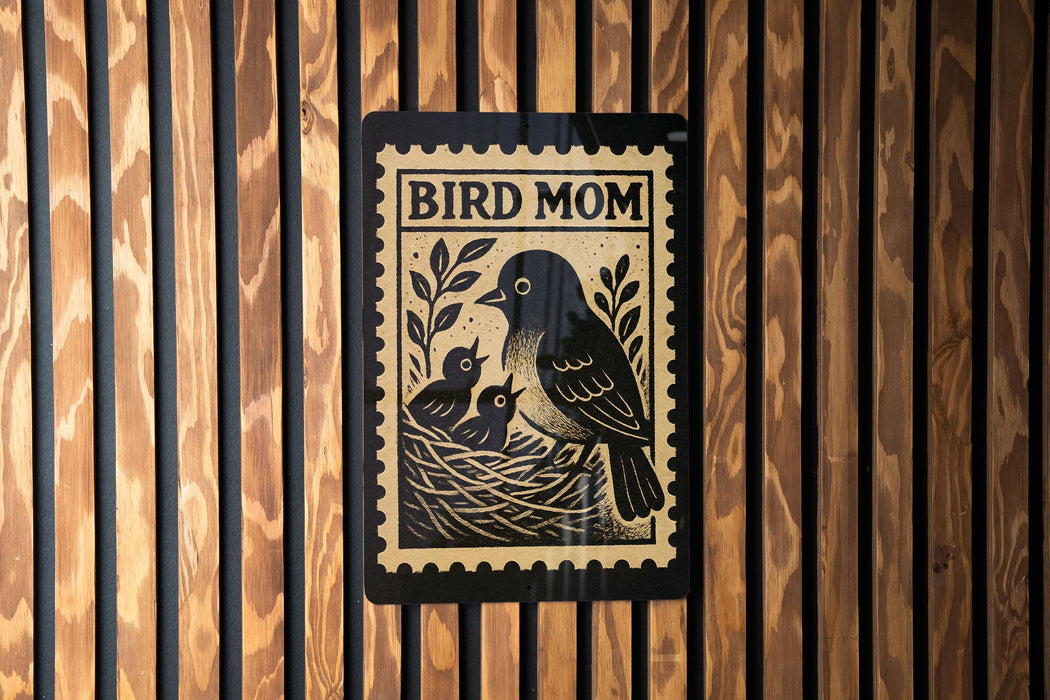 A black and white illustration of a bird, likely a mother bird, with her two young birds in a nest, is displayed on a wooden wall.