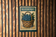 A metal sign with a basket of blueberries mounted on a wooden wall.