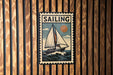 a vintage-style poster of a sailboat on a wave, mounted on a wooden wall.