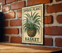 A metal sign with a plant illustration and the text "SPIDER PLANT BASKET" is displayed on a brick wall.