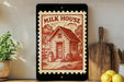 a framed illustration of a small wooden house with a cow in front of it, surrounded by trees and a barn, all set against a rural landscape.