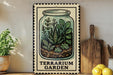 A framed illustration of a terrarium garden, featuring various plants and a glass jar, is displayed on a shelf next to a wooden cutting board and some lemons.