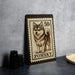 A wooden frame with a postage stamp design featuring a small dog, likely a Pomeranian, on a gray background.