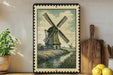 a framed illustration of a windmill on a shelf, surrounded by various kitchen utensils and a potted plant.